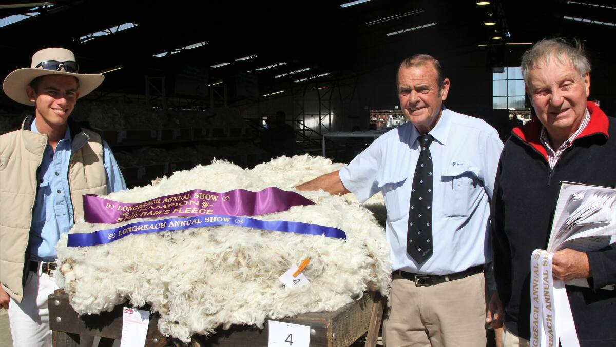 Jed Morrison, Barcaldine Downs, admiring the grand champion fleece at the Longreach Show, exhibited by Victoria Downs, Morven, with Warren Zernike, AWN, under the watchful eye of steward, Tony Neilson.