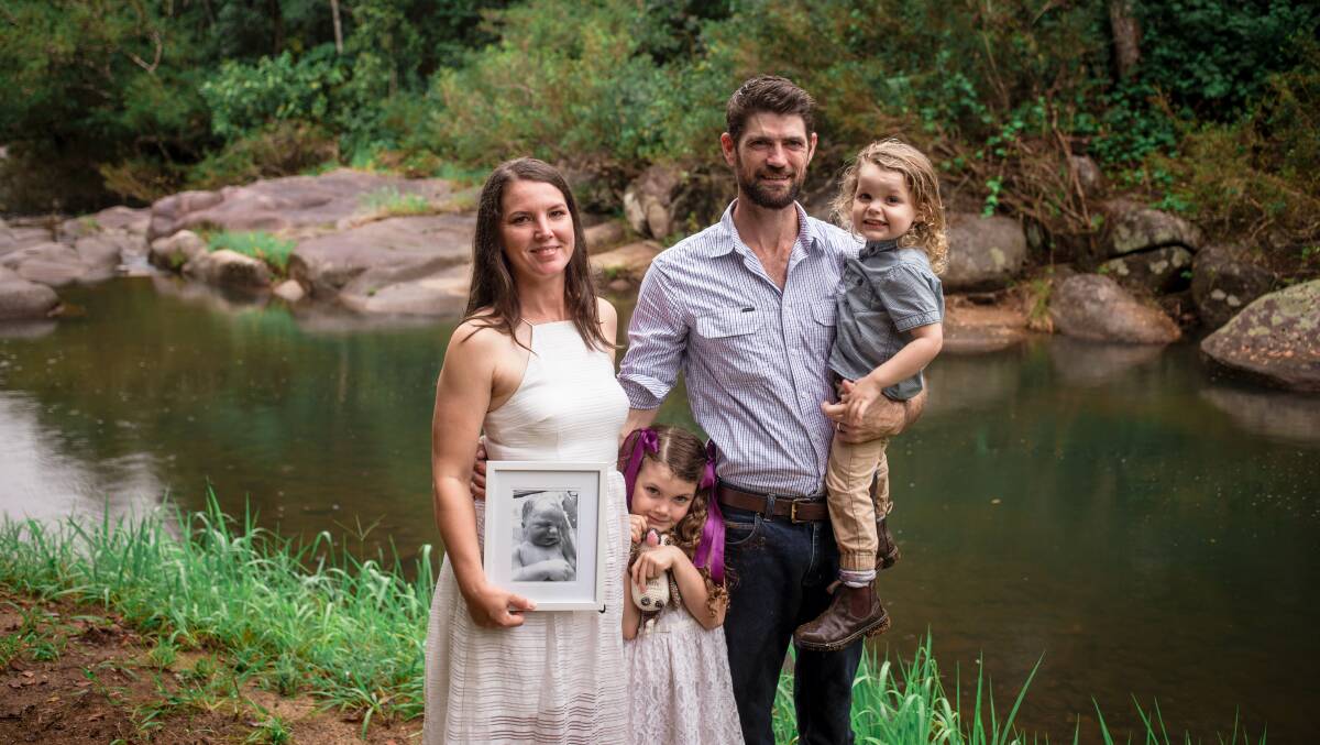 Marina, Clancy, Zach and Banjo White at home at Millaa Millaa. Marina holds a photo of their stillborn son, Henry. Picture by Kelly Butterworth.