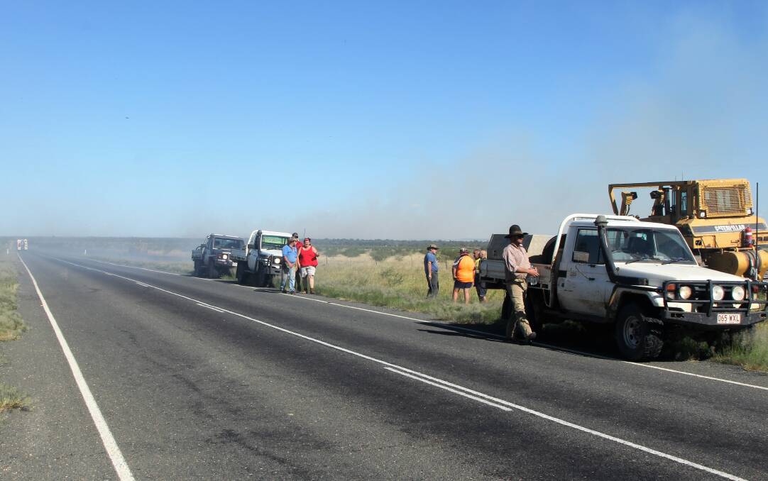Landholders wait with firefighting units on a high point on the Landsborough Highway to ensure no other spot fires break out in the high winds.